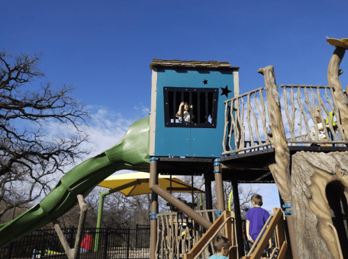 A colorful playground structure with a slide, featuring children playing and a blue sky in the background.