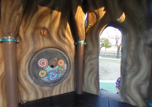 Interior of a playground structure featuring colorful gears and a butterfly on a wooden-like wall.