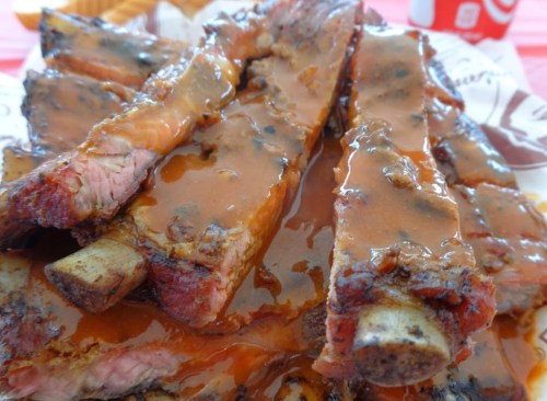 A close-up of juicy, sauced barbecue ribs stacked on a plate, showcasing their smoky texture and rich glaze.