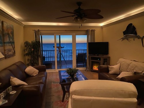 Cozy living room with a view of the ocean at sunset, featuring a sofa, TV, and a telescope by the balcony.