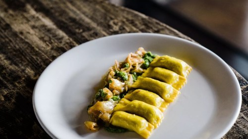 A plate of yellow ravioli with a green sauce, served on a rustic wooden table.