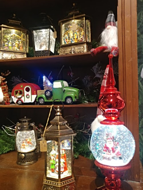 A festive display of decorative lanterns and snow globes featuring Santa, a green truck, and holiday scenes.