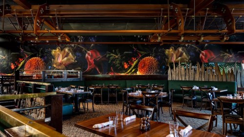 A stylish restaurant interior featuring wooden tables, chairs, and vibrant floral murals on the walls.
