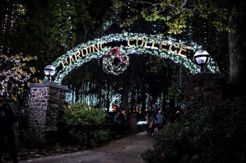 A festive archway reading "Harding College" adorned with lights and a wreath, surrounded by trees and holiday decorations.