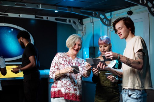 A group of three people, including a woman and two young adults, examine photos together in a brightly lit room.