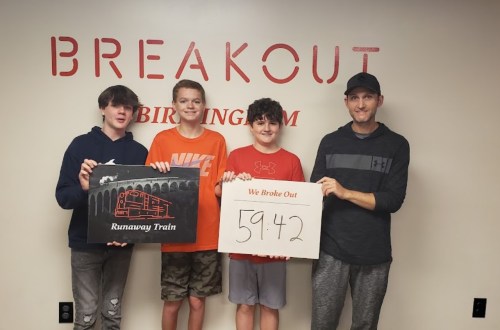 Four people stand in front of a "Breakout" sign, holding signs celebrating their escape from a runaway train challenge.