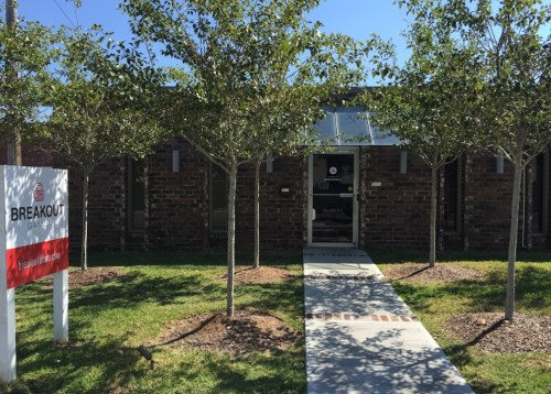 Exterior view of a brick building with a sign reading "BREAKOUT" and a pathway lined with small trees.