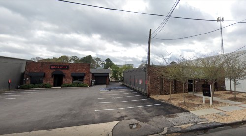 A view of a brick building labeled "Breakout" next to a modern structure, with cloudy skies overhead and empty parking spaces.