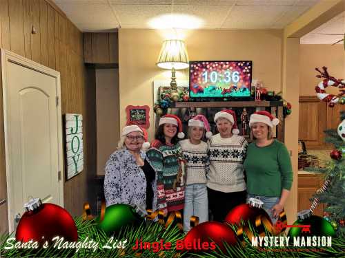 Five women in festive hats pose together in a decorated room with a Christmas theme, smiling at the camera.