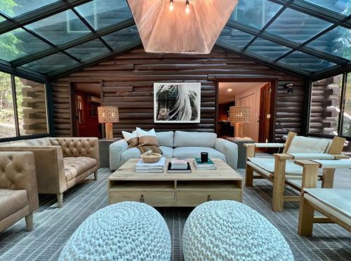 Cozy living room with glass walls, wooden accents, and stylish furniture, featuring a central coffee table and soft lighting.