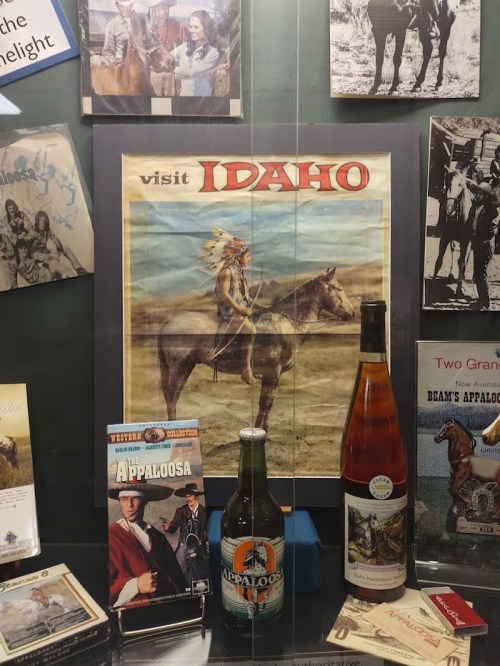 A display featuring a vintage "Visit Idaho" poster, Appaloosa memorabilia, and a bottle of wine and beer.