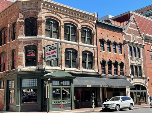 Historic brick buildings with storefronts, including St. Elmo Steak House, under a clear blue sky.
