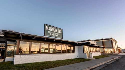 Exterior of Manwaring Handmade Cheese building with a sign, showcasing a modern design and large windows.