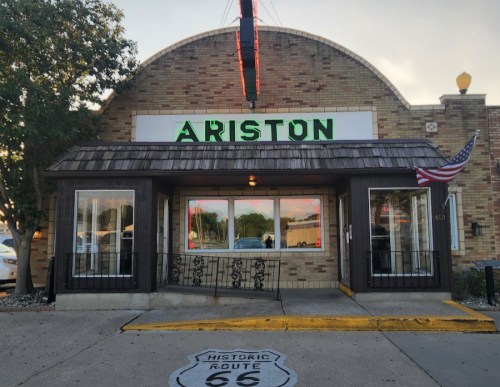 Front view of the Ariston restaurant, featuring a brick facade, neon sign, and an American flag on Route 66.