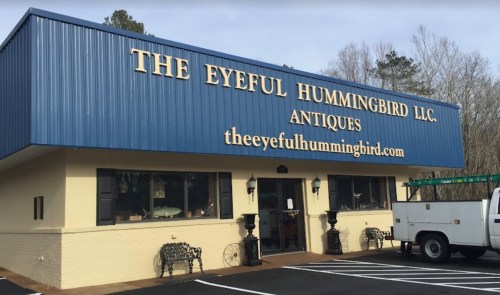 A blue and yellow building with "The Eyeful Hummingbird LLC Antiques" sign and a white truck parked outside.