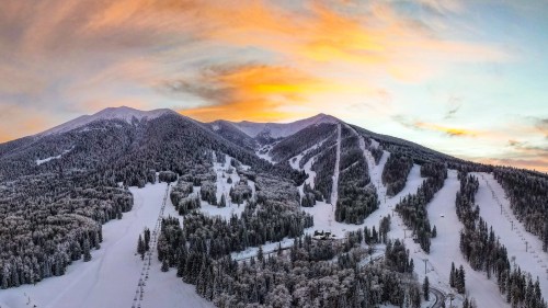 A scenic winter landscape featuring snow-covered mountains and trees under a colorful sunset sky.