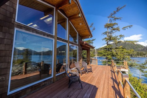 A wooden deck with chairs overlooks a serene lake and mountains under a clear blue sky.