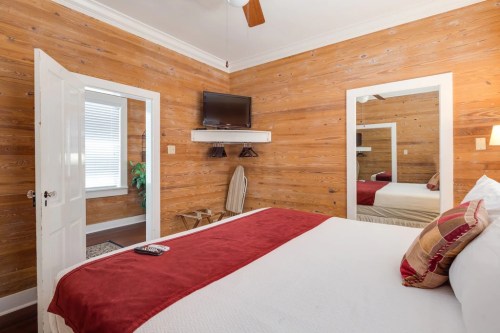 Cozy bedroom with wooden walls, a bed with red accents, a TV, and a mirror reflecting the room.