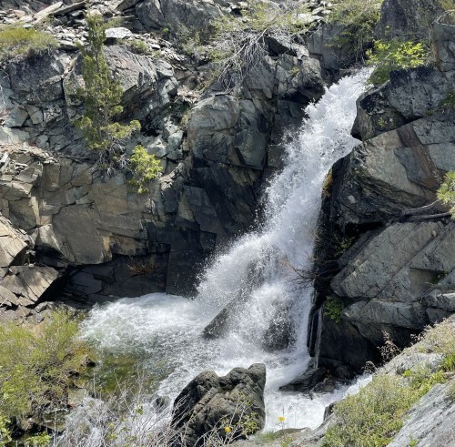 A cascading waterfall flows over rocky terrain, surrounded by greenery and rugged cliffs.