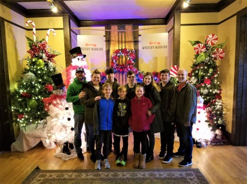 A group of ten people poses together in front of festive holiday decorations, including trees and a snowman.