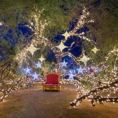 A festive scene with a red chair surrounded by twinkling lights and star decorations in a dark, enchanting setting.