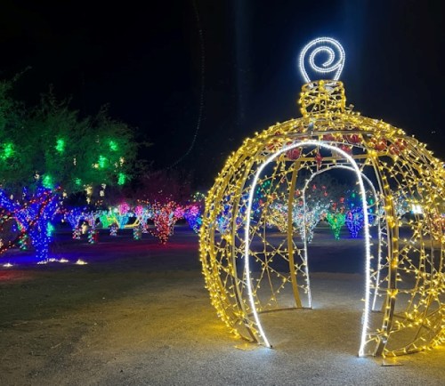 A large, illuminated ornament structure surrounded by colorful holiday lights in a nighttime setting.
