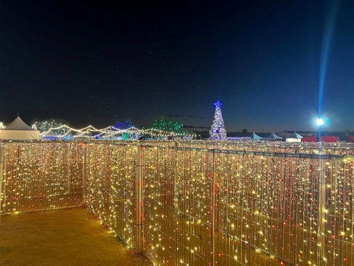 A festive scene at night with colorful lights, a decorated tree, and illuminated pathways creating a holiday atmosphere.