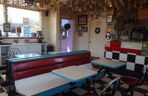 A retro diner interior with checkered floors, red and blue seating, and walls adorned with photos and dollar bills.
