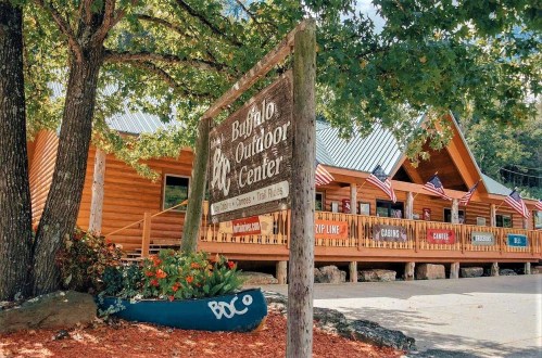 A wooden sign for Buffalo Outdoor Center in front of a rustic building surrounded by trees and flags.