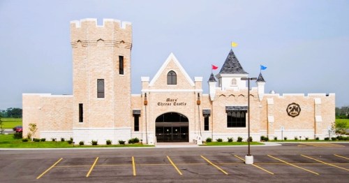 A large, whimsical castle-like building with towers and colorful flags, set against a clear sky.