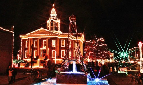 A beautifully lit historic building at night, surrounded by festive lights and a fountain, creating a cheerful holiday atmosphere.