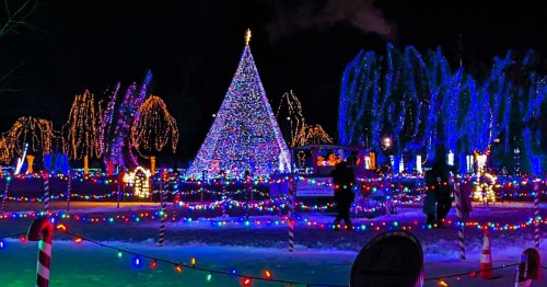 A brightly lit Christmas tree surrounded by colorful lights and decorations in a snowy landscape at night.