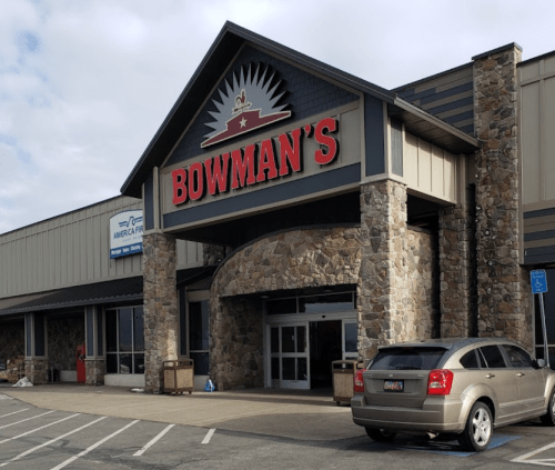 Exterior of Bowman's store featuring a stone facade and large red signage, with a parked car in front.