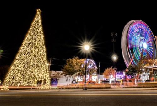 A brightly lit Christmas tree and a colorful Ferris wheel at night, with festive lights illuminating the scene.