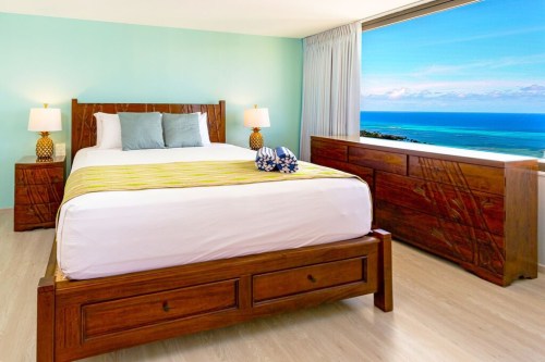 Bright bedroom with a large window showcasing a scenic ocean view, featuring a wooden bed and stylish decor.