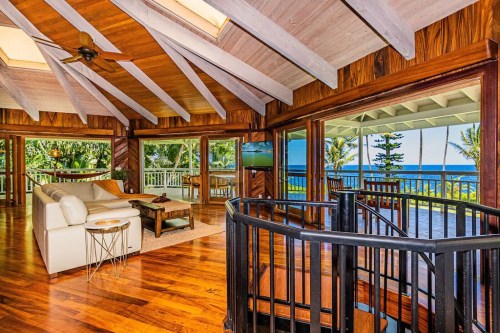 Spacious living room with wooden beams, large windows, and ocean views, featuring a white sofa and a spiral staircase.