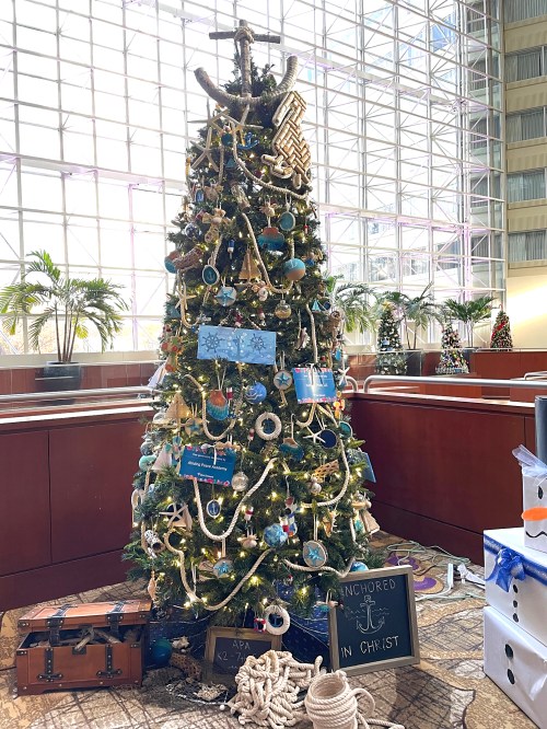 A decorated Christmas tree with nautical themes, featuring blue ornaments, ropes, and a sign reading "Anchored in Christ."