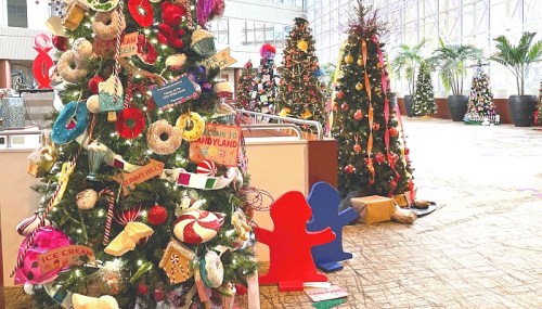 Colorful Christmas trees decorated with playful ornaments and signs, set in a bright, festive indoor space.