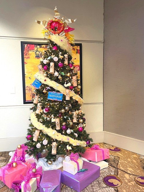 A decorated Christmas tree with colorful ornaments and gifts underneath, set in a festive indoor space.