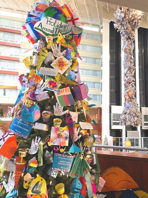A colorful holiday tree decorated with handmade crafts and ornaments, surrounded by festive decorations in a bright space.
