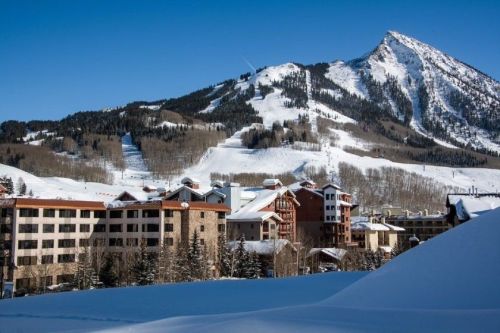Snow-covered mountains rise behind a cozy resort village, with clear blue skies above.