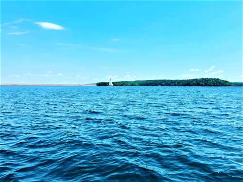 A serene blue lake with gentle waves, featuring a small sailboat near a green island under a clear sky.