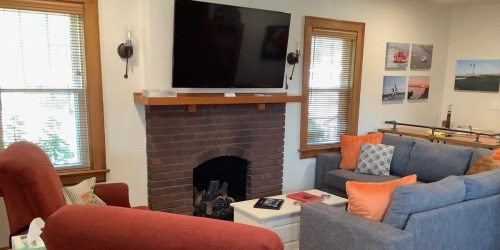 Cozy living room with a TV above a brick fireplace, two sofas, and decorative pillows. Bright and inviting atmosphere.