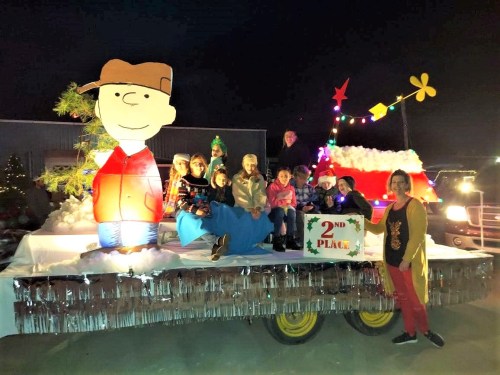 A festive parade float with children and adults, featuring a large Charlie Brown decoration and a "2nd Place" sign.