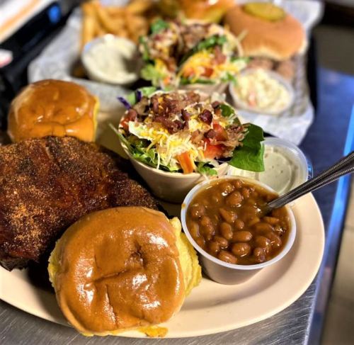 A plate featuring two burgers, a side salad, baked beans, and fries in the background.