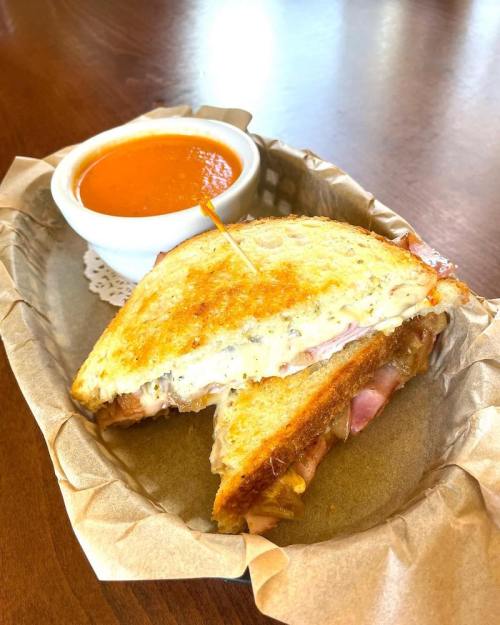 A grilled cheese sandwich with ham, served with a small bowl of tomato soup on a paper-lined tray.