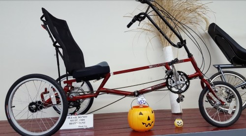 A red recumbent bicycle displayed with a Halloween pumpkin and a sign asking not to sit on it.