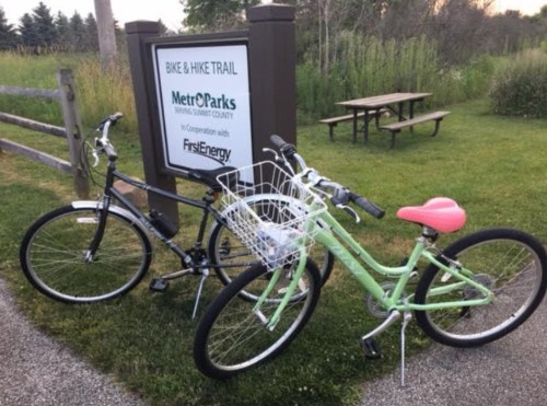 Two bicycles parked near a sign for the MetroParks bike and hike trail, surrounded by greenery.