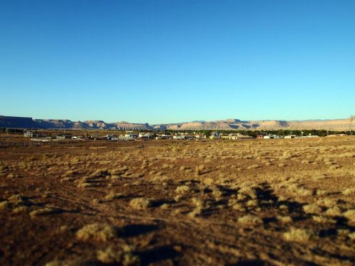 A wide view of a desert landscape with distant mountains and a small town in the foreground under a clear blue sky.