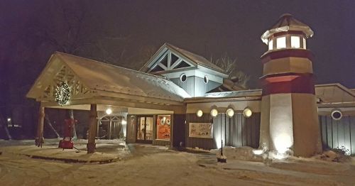 A cozy building with a lighthouse-style tower, decorated for winter, illuminated at night with snow on the ground.